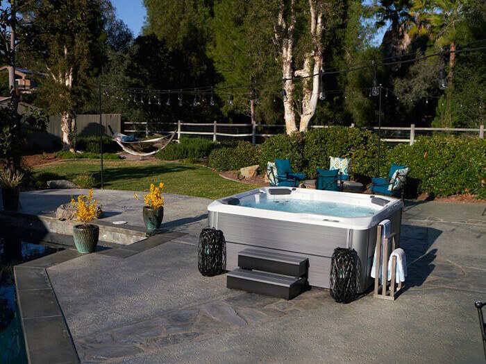 Luxurious outdoor hot tub on a stylish patio, surrounded by cozy seating, decorative lanterns, string lights, and a lush landscaped backyard with a hammock.