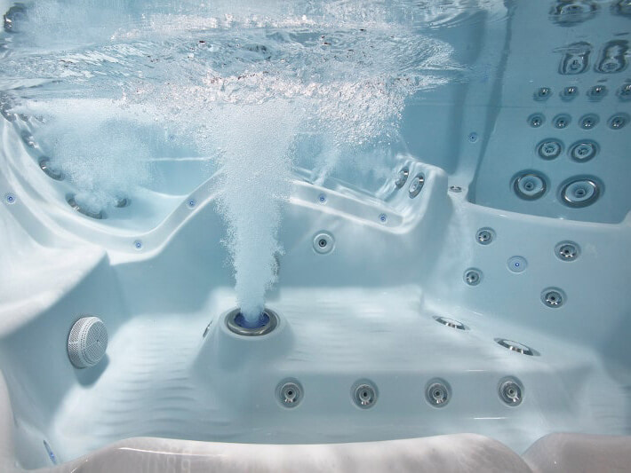 Underwater view of a hot tub with powerful hydrotherapy jets releasing bubbles, surrounded by multiple massage jets and ergonomic seating.