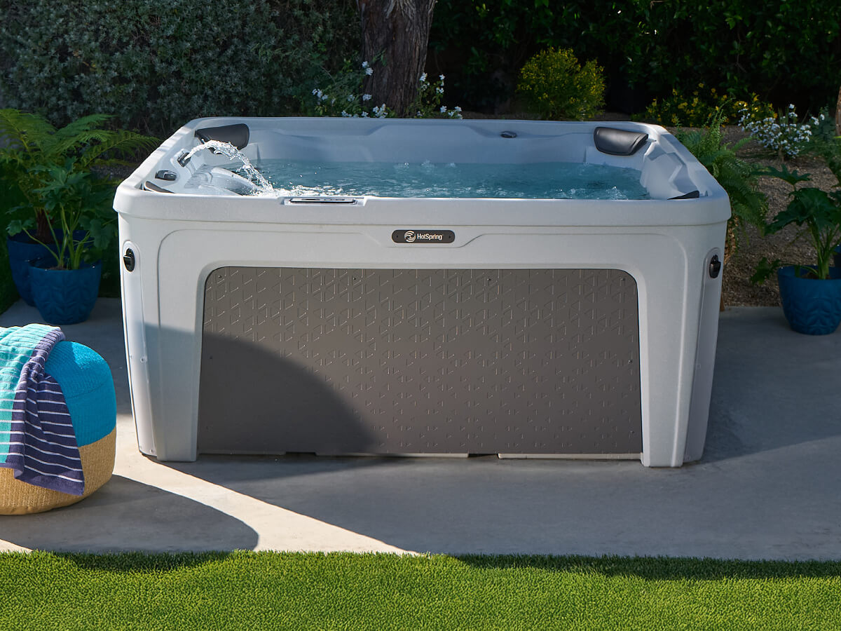 A portable Hot Spring hot tub with bubbling water sitting on an outdoor patio surrounded by greenery