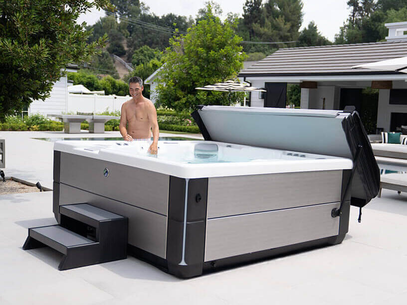 Man opening the cover of a Hot Spring spa installed on a backyard patio
